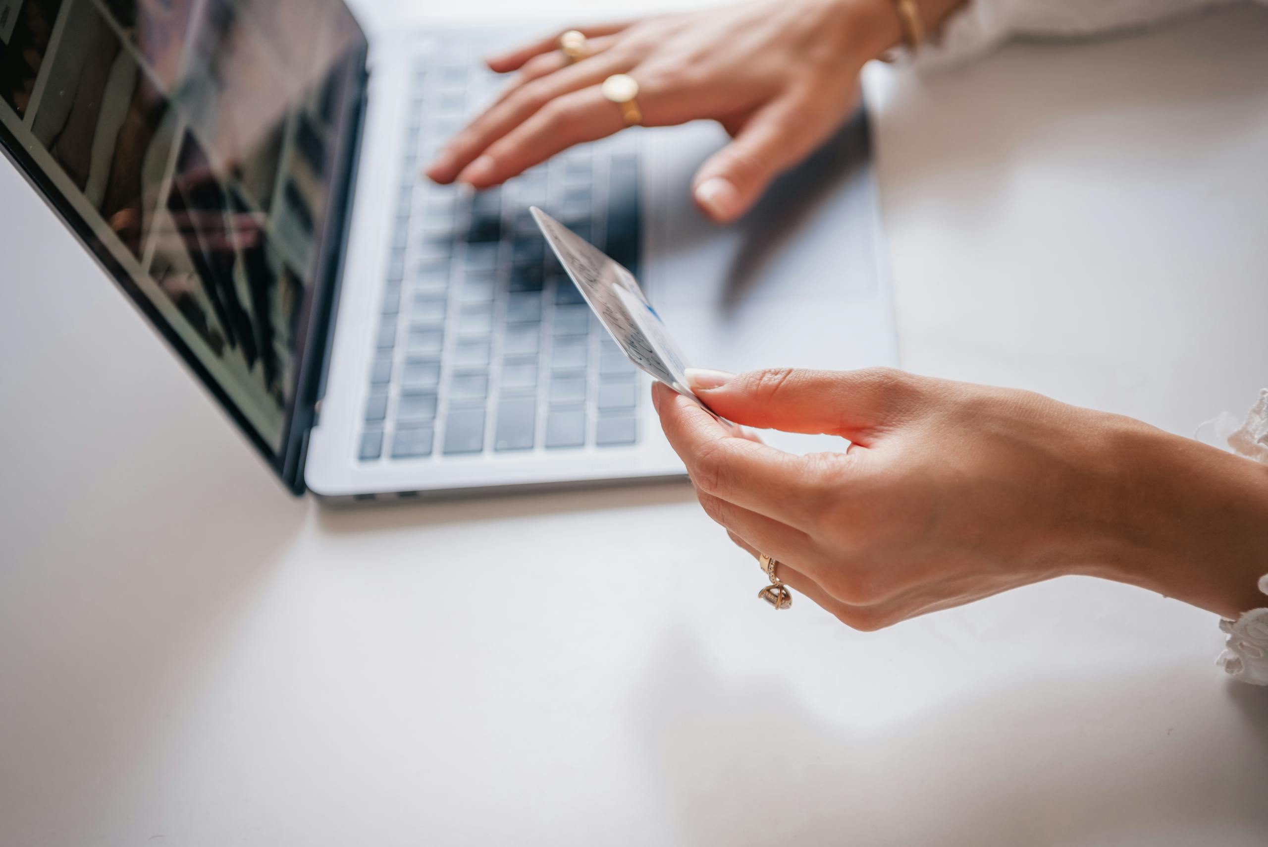 Close-up of woman holding a credit card while typing on a laptop, representing online shopping.